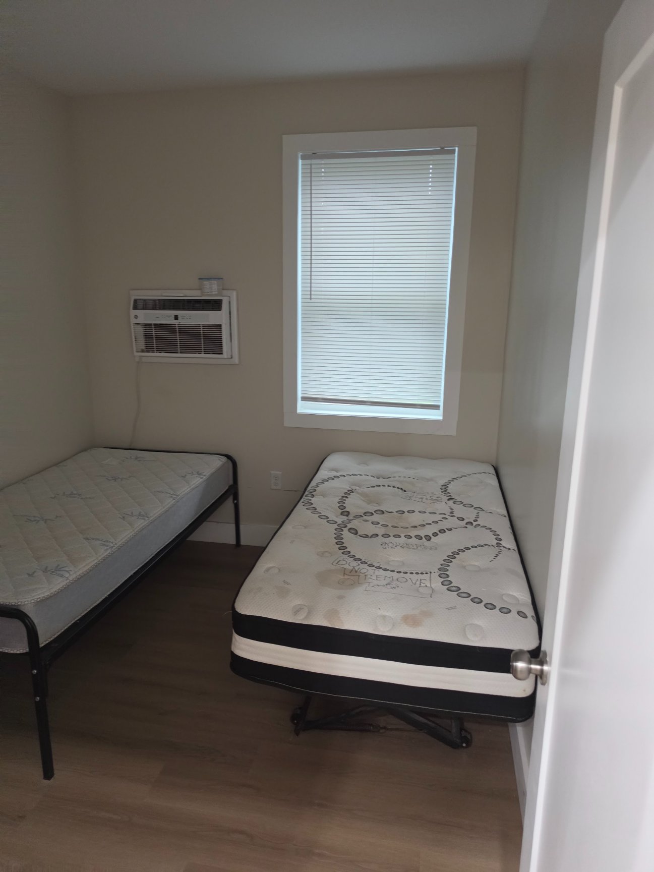 A guest room with two single beds, a window and its own air conditioner